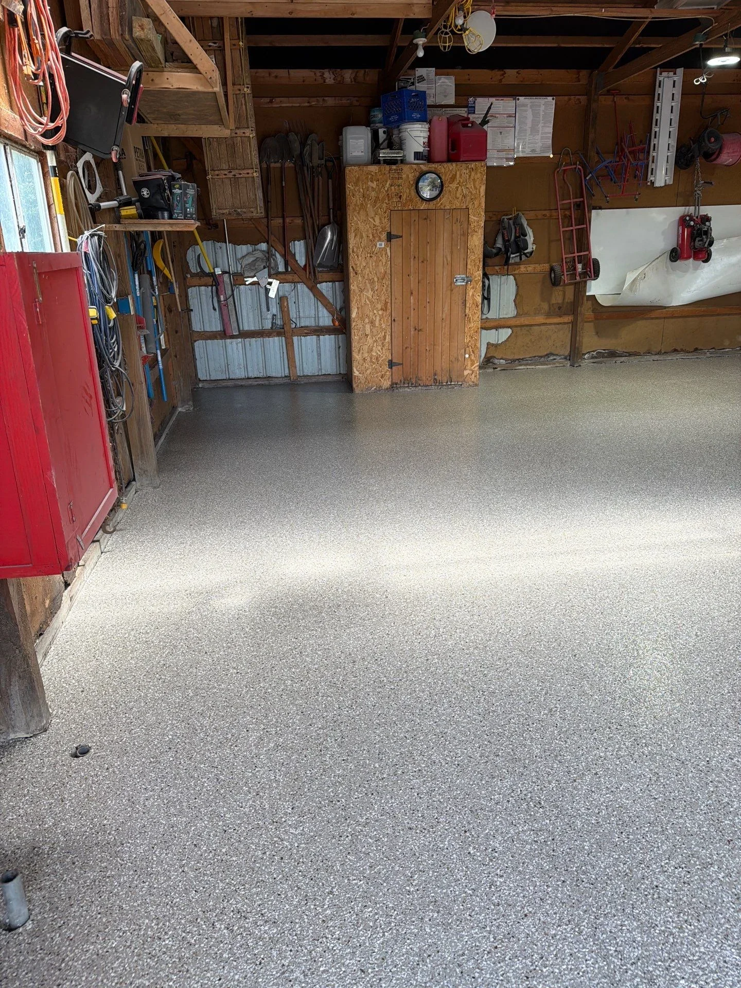 Finished epoxy-coated garage floor with gray speckled finish in wooden-frame garage with storage
