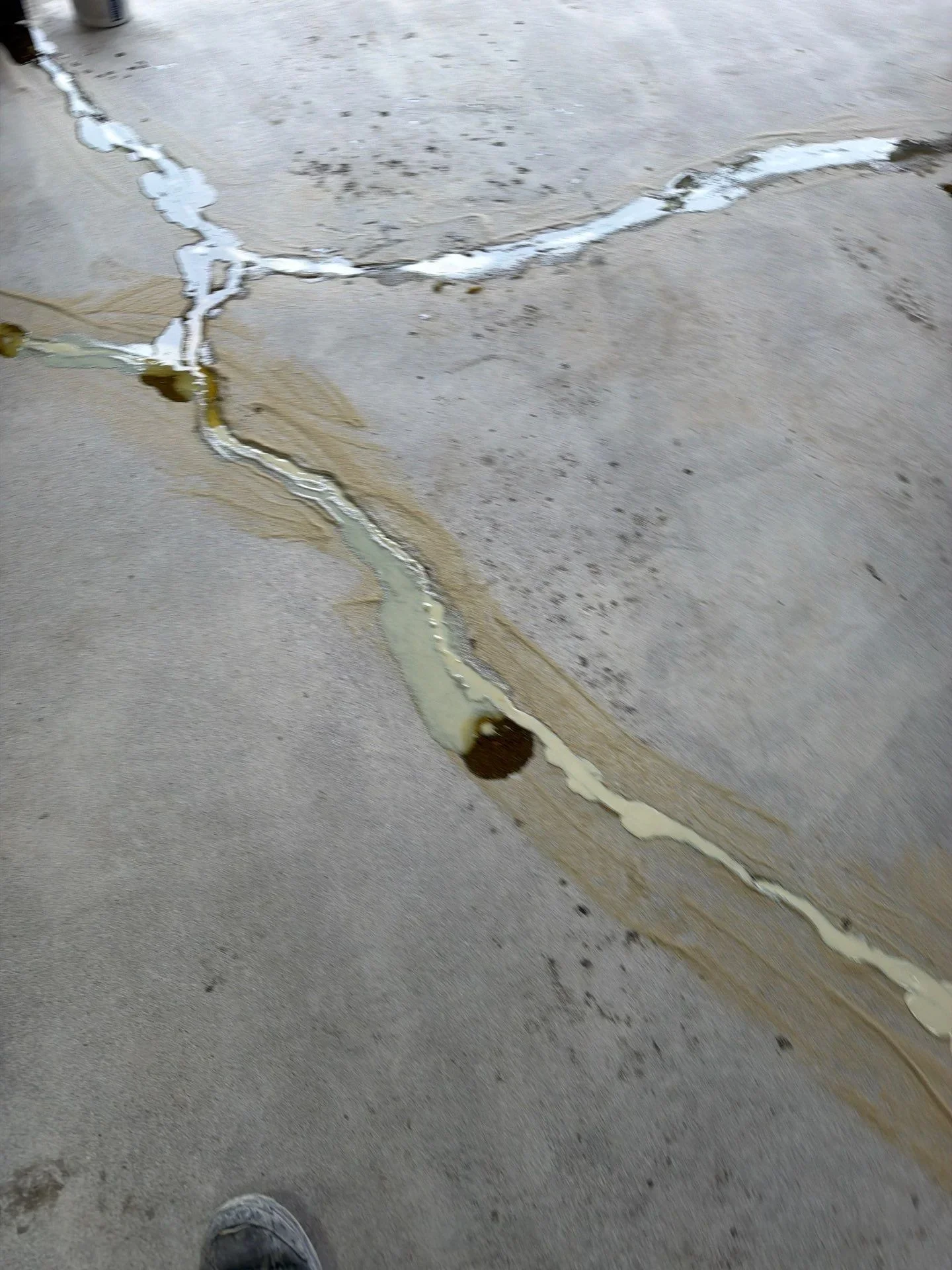 Sealed concrete cracks with white polyurethane filler on gray concrete surface