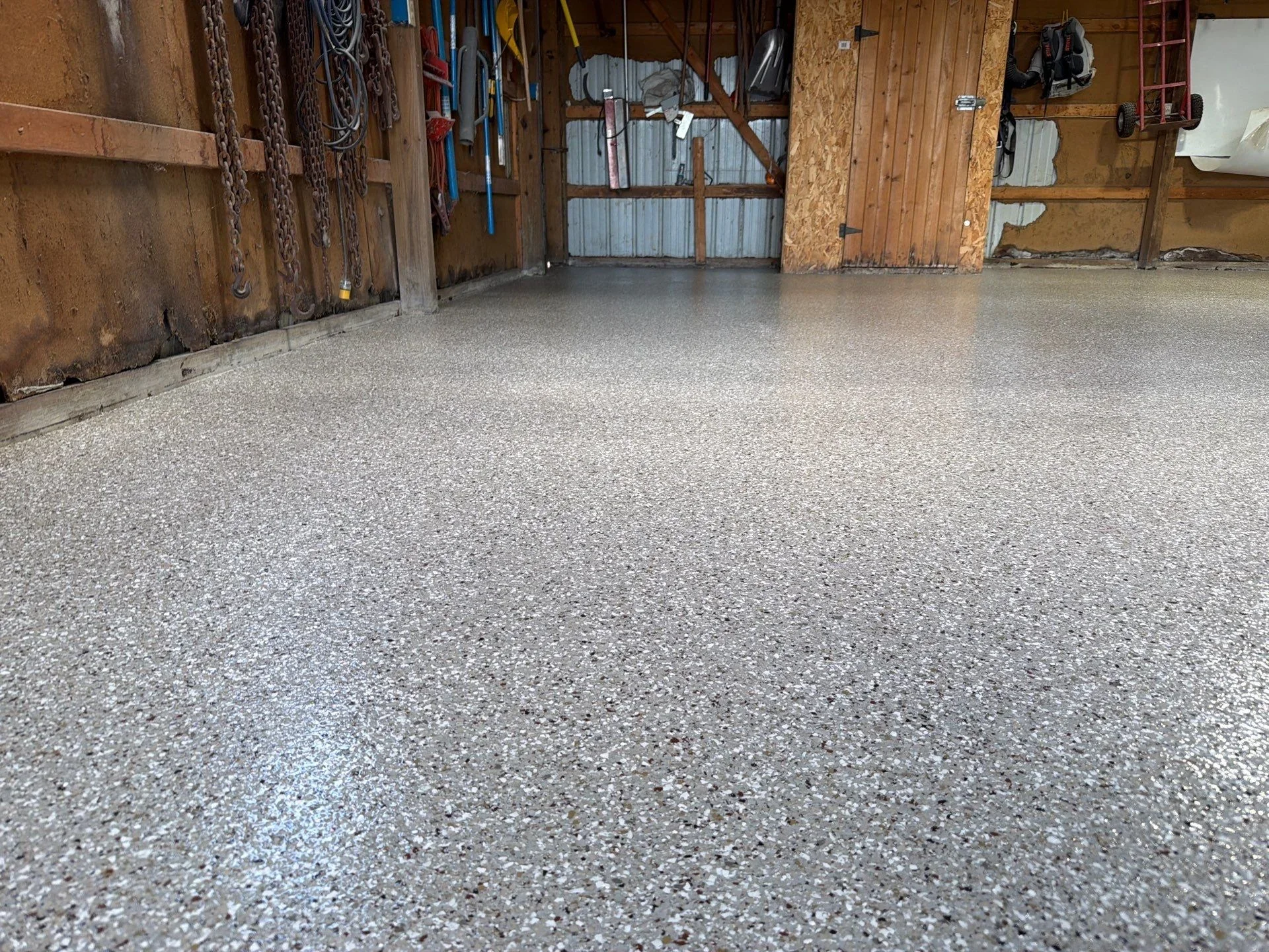 Finished epoxy-coated garage floor with light gray aggregate texture in working garage space