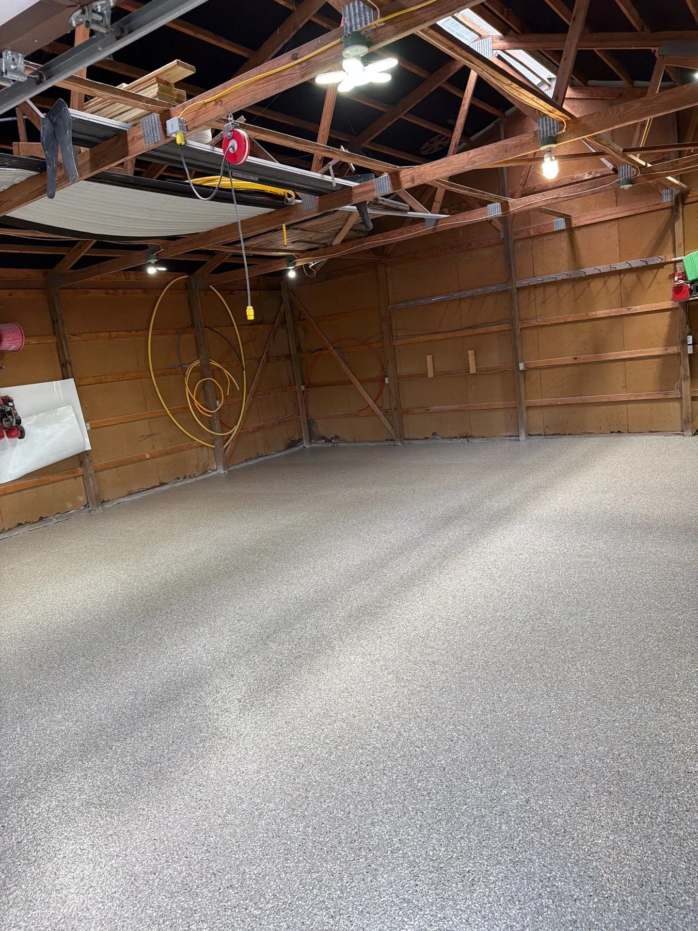 Gray epoxy-coated garage floor with wooden beam ceiling and recessed lighting