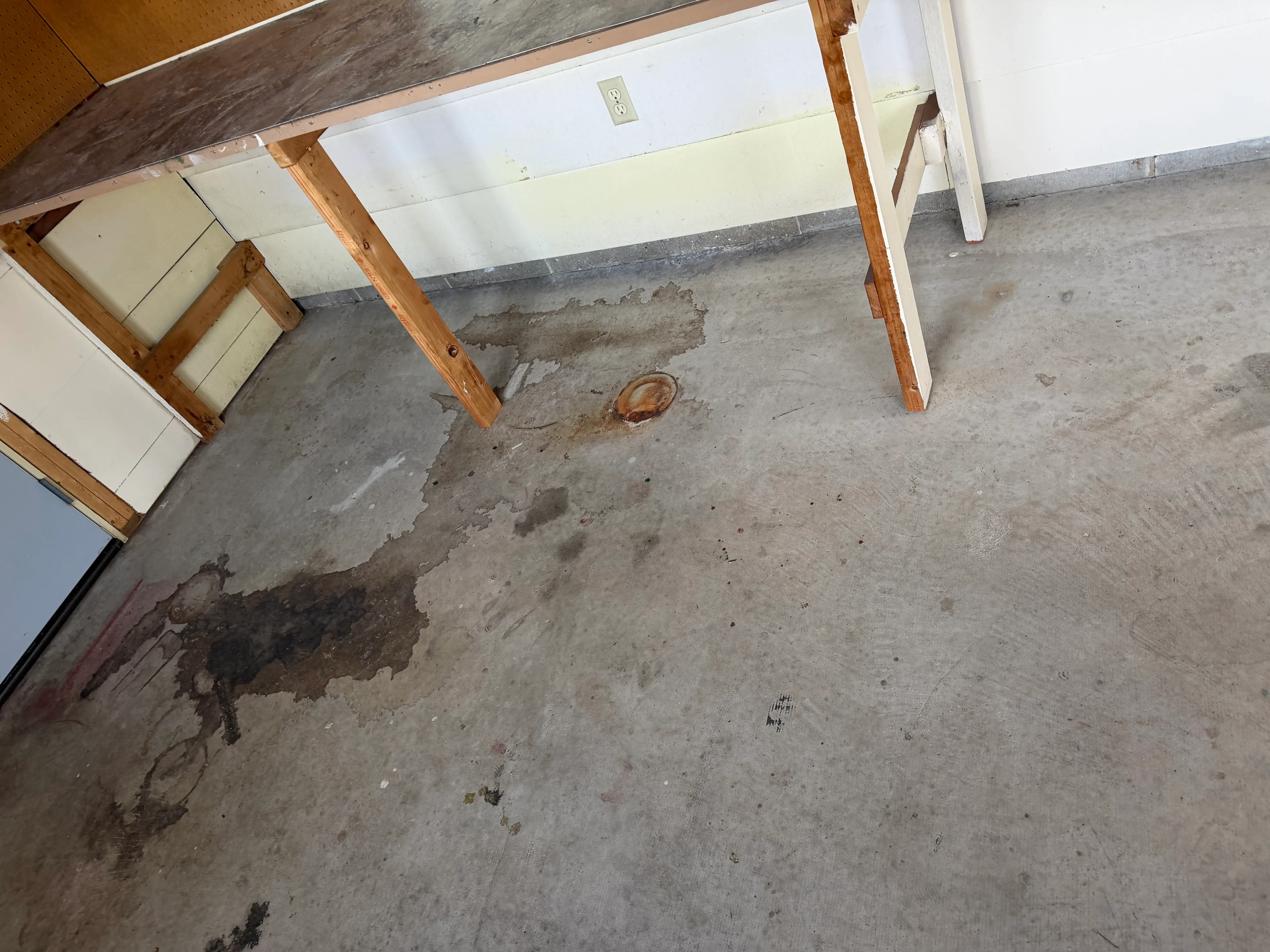 Damaged concrete floor with water stains, exposed wooden support posts, and deteriorated surface areas