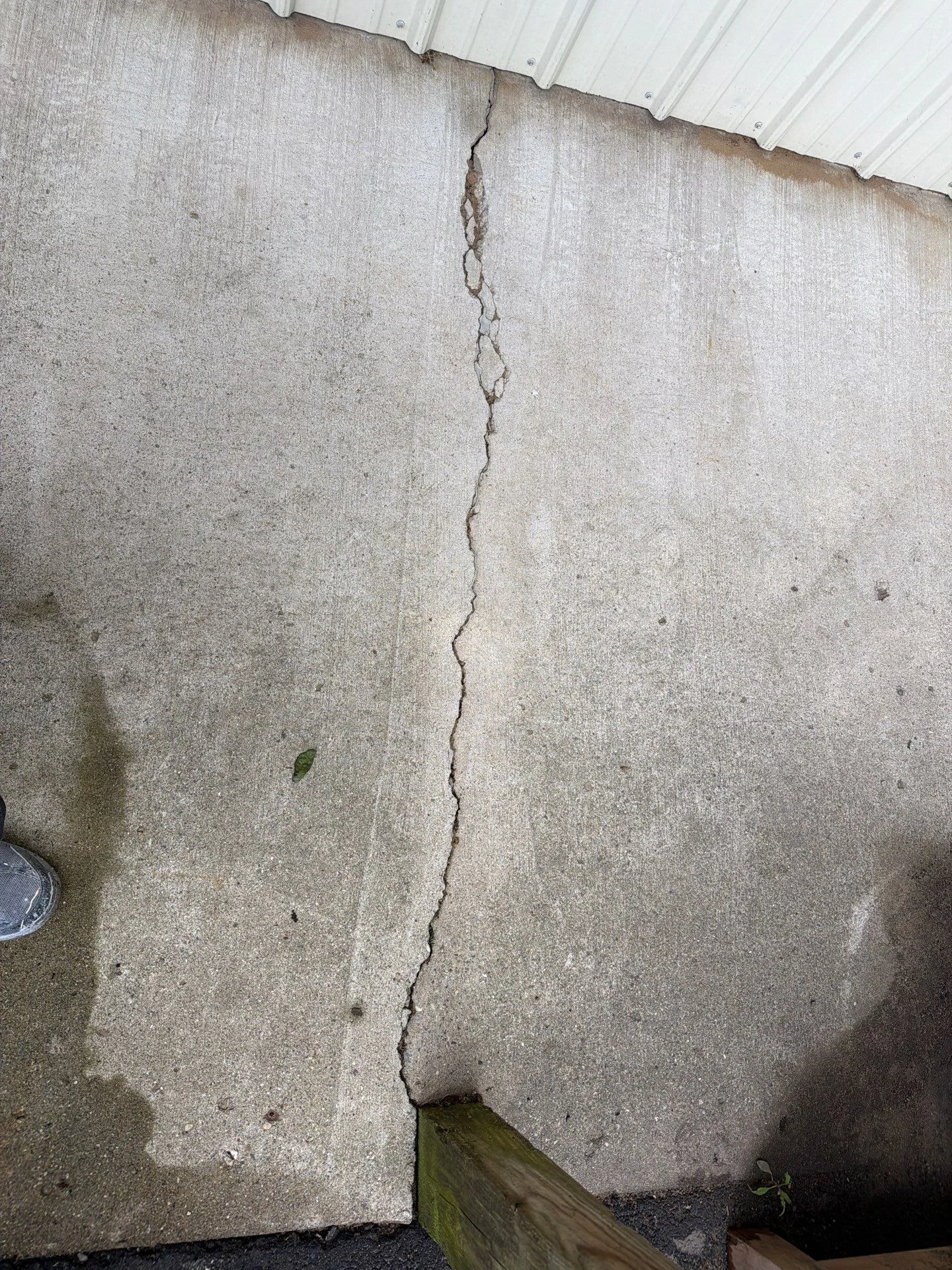 Vertical crack in concrete foundation wall with metal roof trim visible at top