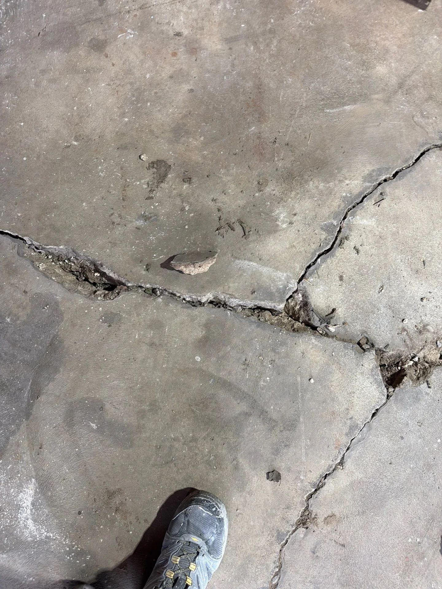 Cracked and spalled concrete surface with active damage lines and debris