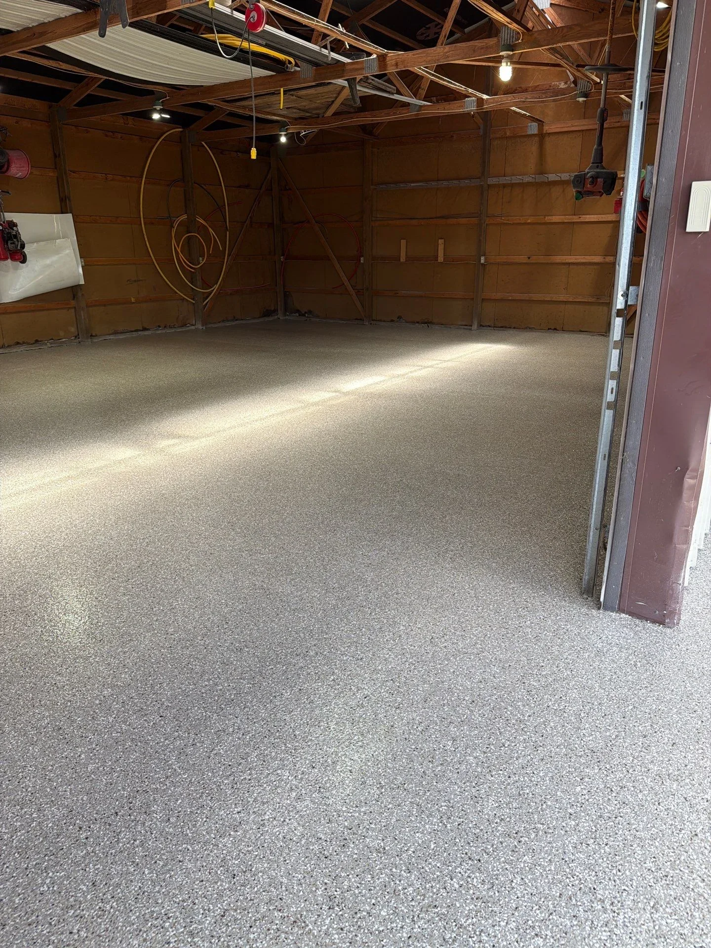 Finished garage floor with gray speckled epoxy coating, wooden walls and exposed beam ceiling
